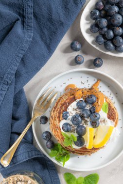 Sağlıklı yaz kahvaltısı, taze böğürtlen, limon, yoğurt ve fıstık ezmeli ev yapımı Amerikan krepleri. Sabah açık gri taş arka plan.