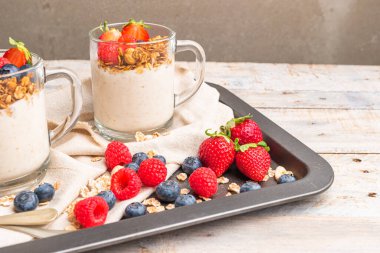 Kavanozda fındıklı, yoğurtlu ve kırmızı meyve meyveli granola. Müsli, yoğurt, kırmızı meyve ve bal ile kahvaltı, beyaz mutfak arka planı..