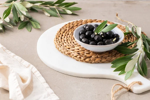 Black olives with olive leaves in ceramic bowl on kitchen countertop
