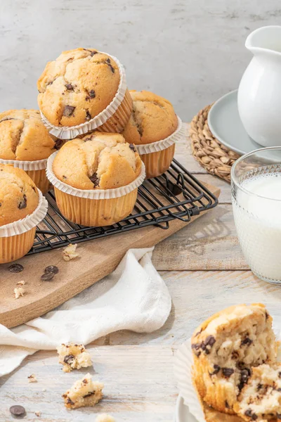 Chocolate chip muffins on a baking rack and glasses of milk on a white kitchen countertop.  Morning breakfast table