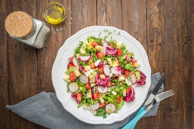 Karışık yeşillik, turp, peynir ve domates ahşap arka plan üzerine bir tabak içinde taze salata. İtalyan Akdeniz veya Yunan mutfağı. Vejetaryen vegan gıda