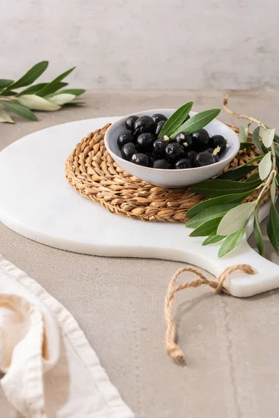 Black olives with olive leaves in ceramic bowl on kitchen countertop