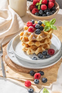 Geleneksel Belçika waffleları, mutfak tezgahına taze ahududu ve yabanmersini serpiştirilmiş pudra şekeri serpiştirilmiş..