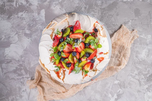 Pavlova cake with cream and fresh summer berries and kiwi on wooden background. Close up of Pavlova dessert with forest fruit and mint. Food photography