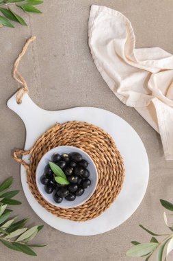 Olives with olive leaves in ceramic bowl on kitchen countertop. Top-view.