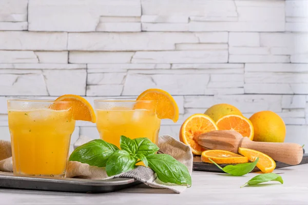 Healthy juice from oranges with basil leaves in glass, selective focus