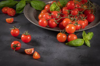 Rustik arka plan üzerinde küçük kırmızı kiraz domates. Kiraz domates üzerinde asma witb fesleğen yaprakları