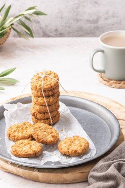 Stack of homemade oatmeal cookies, healthy breakfast cereal oat crackers and mug of milk with coffee on white kitchen countertop