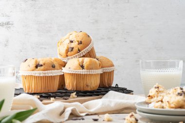 Chocolate chip muffins on a baking rack and glasses of milk on a white kitchen countertop.  Morning breakfast table