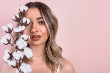 Açık pembe arka planda elinde pamuk bir dal tutan genç ve güzel bir kız.