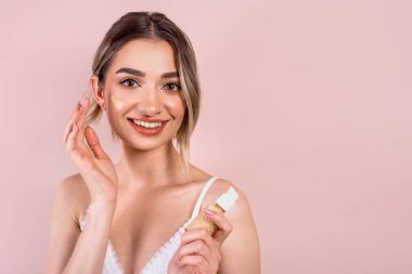 Hafif makyajlı güzel bir kız, elinde akışkan bir temel tutuyor.