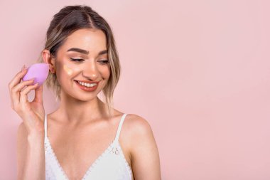 Açık pembe arka planda doğal makyajı olan güzel sarışın kız ellerinde ve temelinde güzellik blenderi süngeri olan, boşluğu kopyalayan kız.