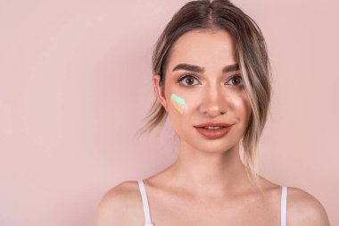 Yüzünde temeli olan pembe bir arka planda hafif makyajlı nazik bir kız.