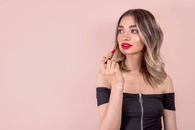 Kırmızı dudakları ve pembe arka planda kırmızı ruju olan sarışın genç bir kadın.