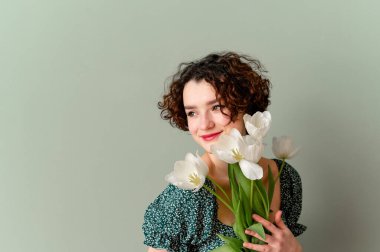 Güzel kız gizemli bir şekilde elinde beyaz lalelerle gülümsüyor.