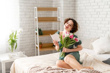 Elinde bir buket lale tutan ve yatakta oturan güzel sürpriz esmer kız.