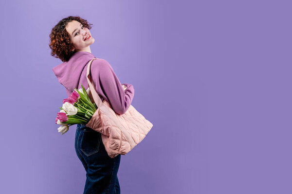portrait of a curly girl with tulips in the photo studio on a purple background. Copy space