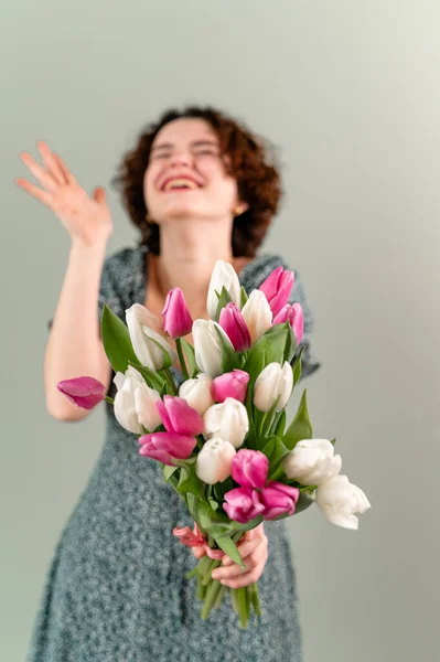 Bella adolescente con riccioli su uno sfondo grigio che tiene un mazzo di tulipani. Focus selettivo — Foto Stock