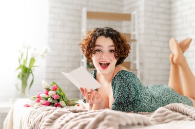 Şaşırdım, güzel esmer kadın yatakta yatar ve bir kart okur.