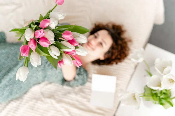 Menina morena bonita deitada na cama com tulipas. FÓCIO SELECTIVO — Fotografia de Stock
