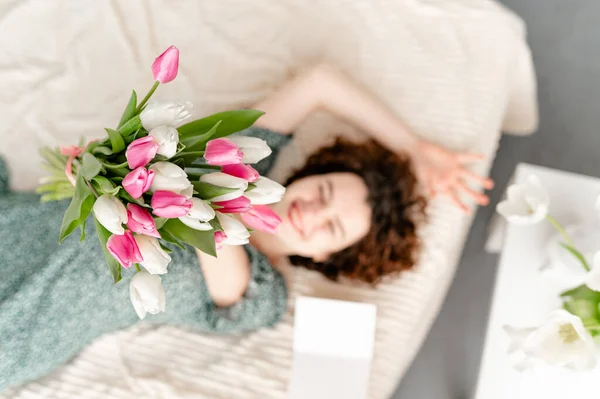 Menina morena bonita deitada na cama com tulipas. FÓCIO SELECTIVO — Fotografia de Stock