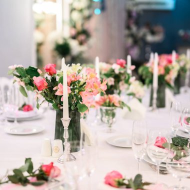 Bahçede romantik bir buluşma sırasında şarap kadehlerinin yanına yuvarlak güller konmuş mum ve vazo.