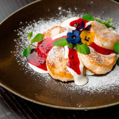 Pudra şekeri serpilmiş ve çiçeklerle süslenmiş cheesecake tatlısı, kahvaltı tabağı.