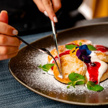 Pudra şekeri serpilmiş ve çiçeklerle süslenmiş cheesecake tatlısı, kahvaltı tabağı.