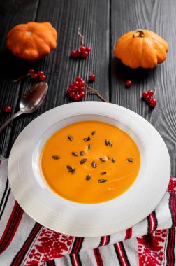 Balkabağı tohumlarıyla süslenmiş siyah bir masada beyaz bir tabakta kabak çorbası. en üstteki görünüm