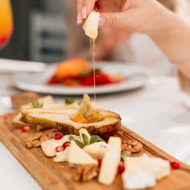 Armut ve fındıkla süslenmiş tahtanın üzerinde bal bulunan farklı peynir türleri.