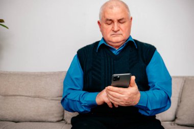 Oturma odasındaki koltukta oturan sıradan bir adam cep telefonuyla interneti ve dizüstü bilgisayarları karıştırıyor. Bilgisayarla çalışan ve evden akıllı telefon kullanan serbest çalışan biri..