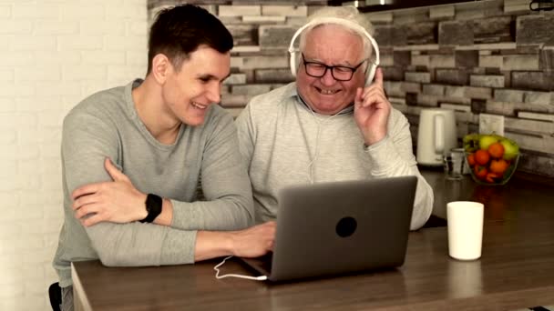 祖父とソファに座ってノートパソコンの使い方を教えている孫 幸せな家族は自宅でソファでリラックスし 現代のコンピュータを一緒に使用し インターネットを閲覧し ゲームをプレイし 映画を見る — ストック動画