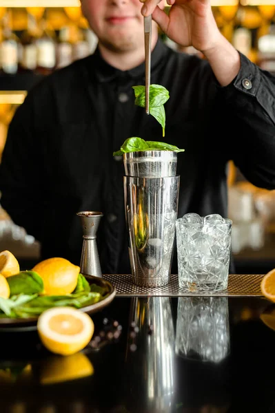 a glass with ice cubes on the bar. bartender prepares a cocktail mohito