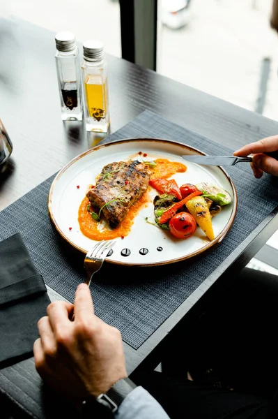 a man dines in a restaurant baked meat with vegetables