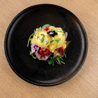 Tahta masada, siyah tabakta servis edilen sıcak sığır eti salatası. Kızarmış dana madalyonu, kabak dilimleri, kiraz domatesleri, parmesan peyniri ile servis edilen marul..