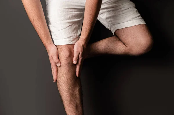 young sport man with strong athletic legs holding knee with his hands in pain isolated on white background