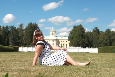 Genç bir kadın çimenlerde oturuyor.