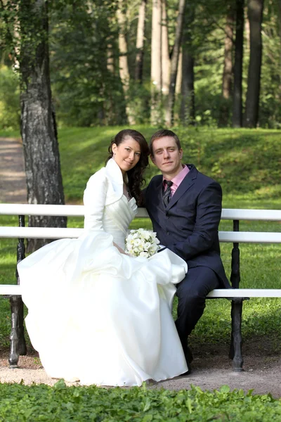 Bride and groom sitting on bench in park — Stock Photo, Image