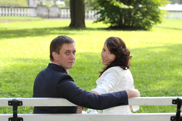 Bride and groom sitting on bench in park — Stock Photo, Image