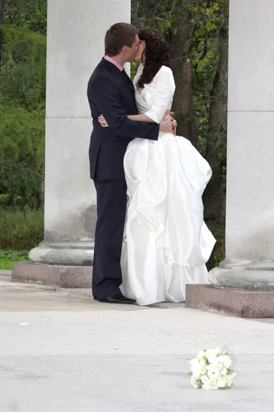 Bride and groom kissing near columns in park — Stock Photo, Image