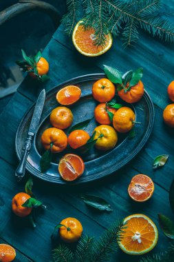 Tangerines with green leaves on a green wooden table in a rustic style surrounded by spruce branches