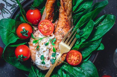 Taze çiğ ıspanak ve kızarmış somon, domates ve krem peynir soslu bir tabak. 