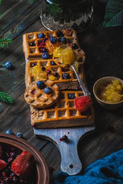 Kruvasan Waffle ya da çilek ve yaban mersini soslu koyu arkaplanda servis edilen Croffle. Kapat, boşluğu kopyala.