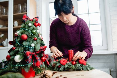  Dekoratör atölyedeki ladin dalları ve kırmızı mumlardan Noel süsü yapıyor.. 