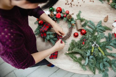 Dekoratör masanın üzerindeki ladin dallarından yapılmış bir Noel süslemesine İskoç kumaşı bir fiyonk bağlar. Üst görünüm