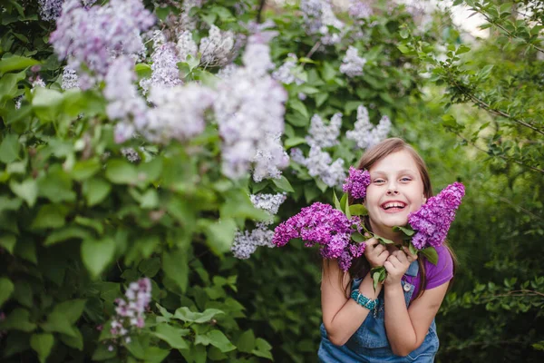 Ridere europeo bruna ragazza con lilla fiori in mano e capelli in un estate lilla giardino — Foto Stock