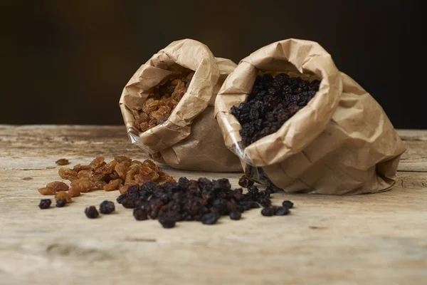 Golden and black raisins in paper bags on a wooden table — Stock Photo, Image