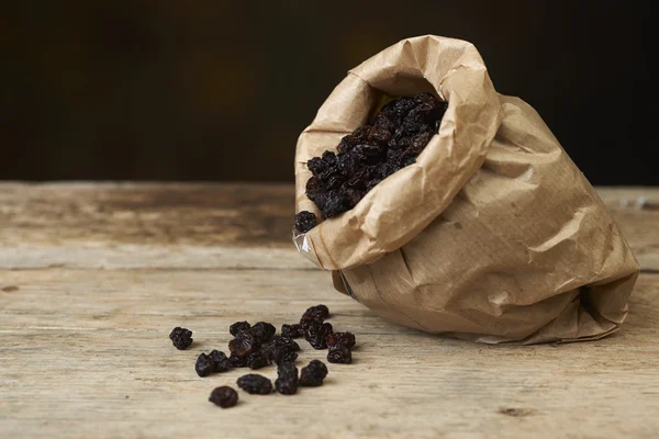 Raisins noirs dans des sacs en papier sur une table en bois — Photo