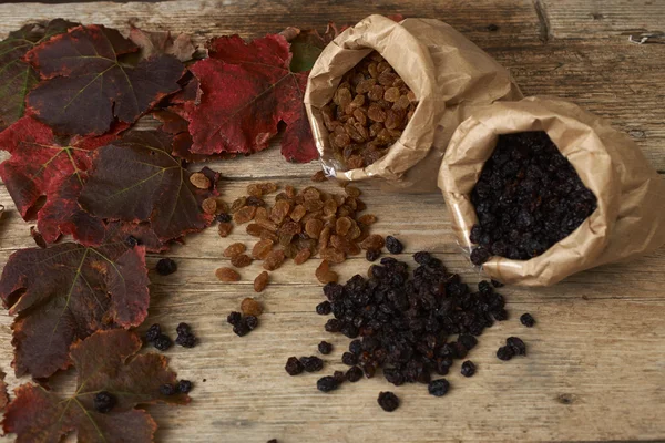 Uva passa dorata e nera in sacchetti di carta su un tavolo di legno — Foto Stock