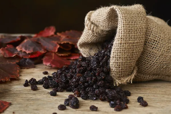 Black raisins in burlap bag over wooden table — Stock Photo, Image